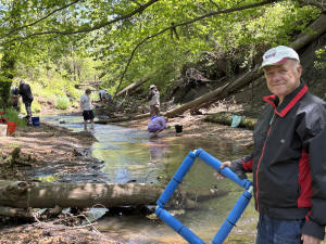 Longtime member in a red jacket holding a blue screen frame in the creek